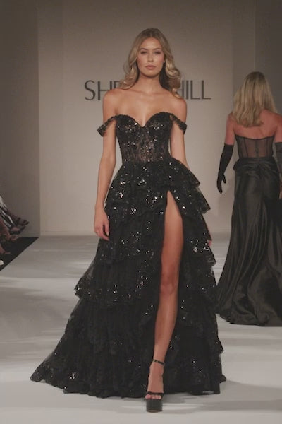 A captivating tulle sequin A-line gown with a sheer corset bodice, off-the-shoulder straps, and a ruffle high slit skirt. Ideal for prom, red carpet events, and pageants.  This is a video of the model walking down the runway wearing style number 55500.
