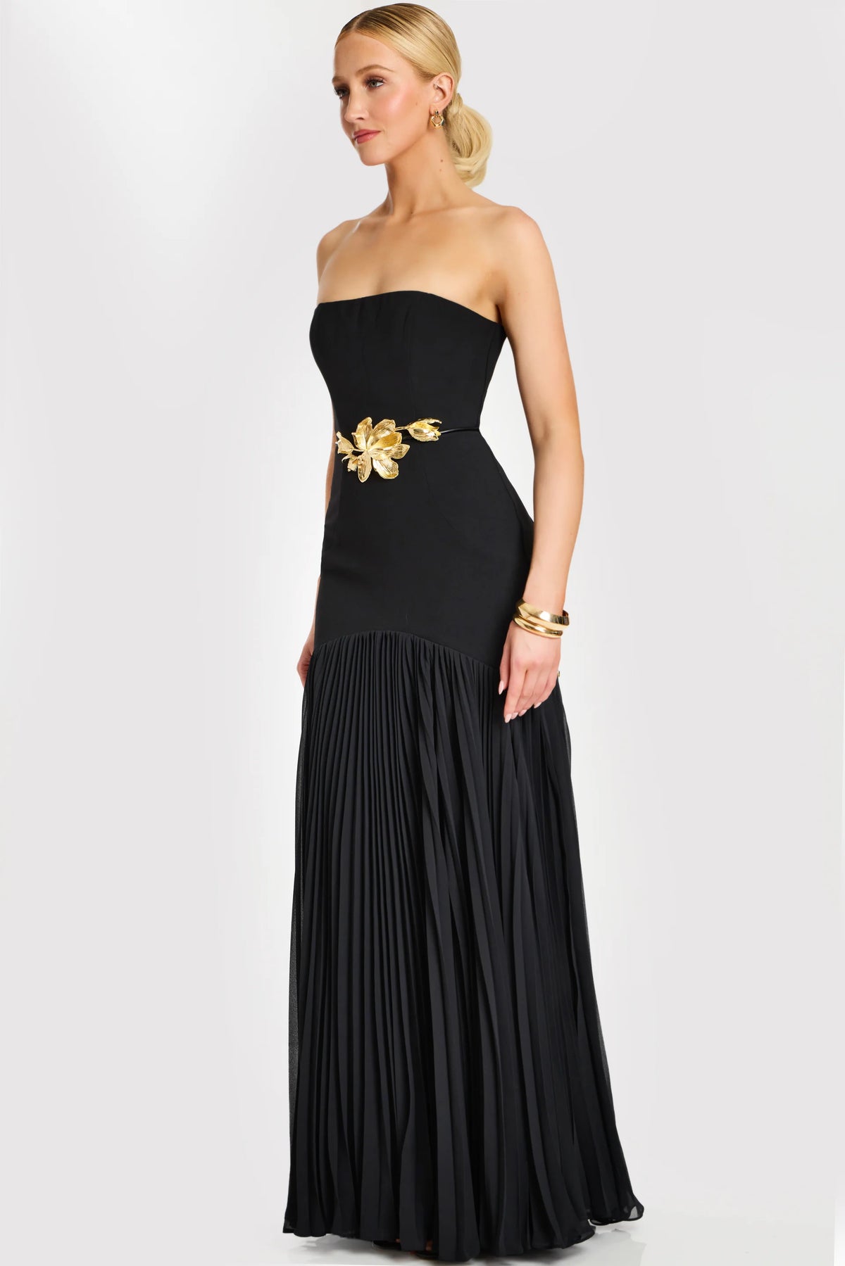 Model wearing Jovani 47000 strapless evening gown with floral waist detail and flowing pleated skirt.