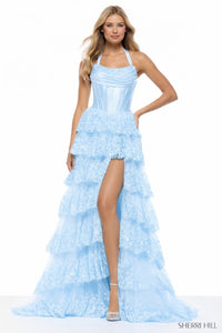 Woman wearing a light blue evening gown with ruffled layers and a high slit on a white background.