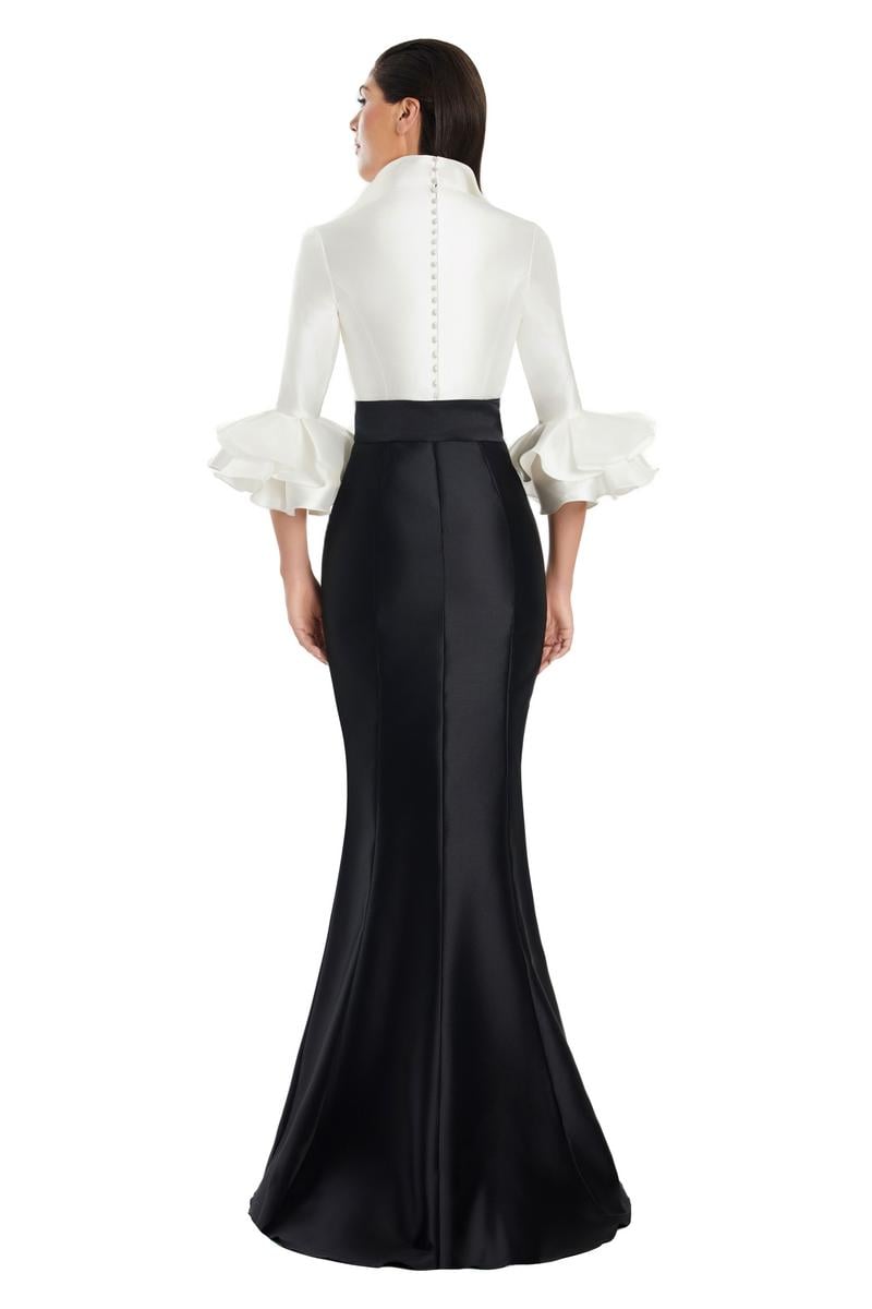 Model wearing Alexander by Daymor 3087S25 gown with mermaid skirt and high-neck jacket featuring dramatic ruffle sleeves and waist sash.