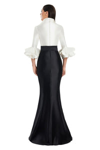 Model wearing Alexander by Daymor 3087S25 gown with mermaid skirt and high-neck jacket featuring dramatic ruffle sleeves and waist sash.