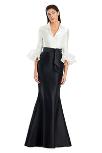 Model wearing Alexander by Daymor 3087S25 gown with mermaid skirt and high-neck jacket featuring dramatic ruffle sleeves and waist sash.