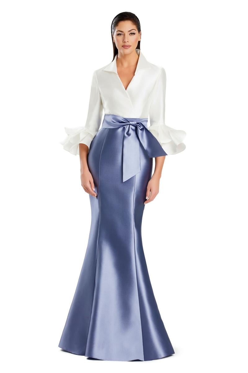 Model wearing Alexander by Daymor 3087S25 gown with mermaid skirt and high-neck jacket featuring dramatic ruffle sleeves and waist sash.