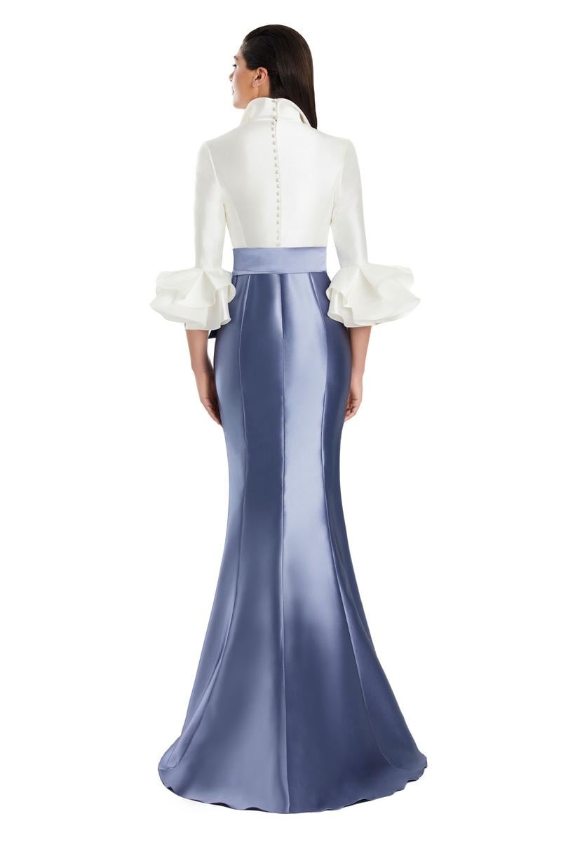 Model wearing Alexander by Daymor 3087S25 gown with mermaid skirt and high-neck jacket featuring dramatic ruffle sleeves and waist sash.