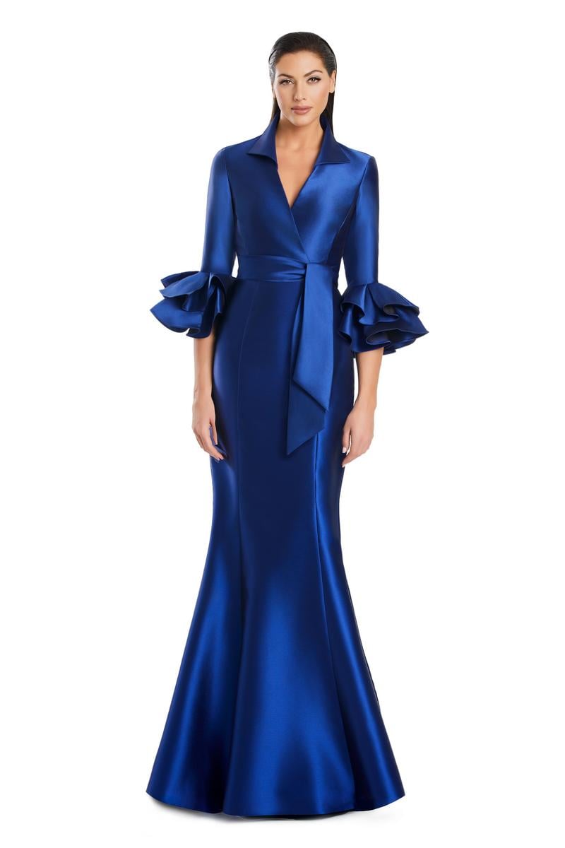 Model wearing Alexander by Daymor 3087S25 gown with mermaid skirt and high-neck jacket featuring dramatic ruffle sleeves and waist sash.