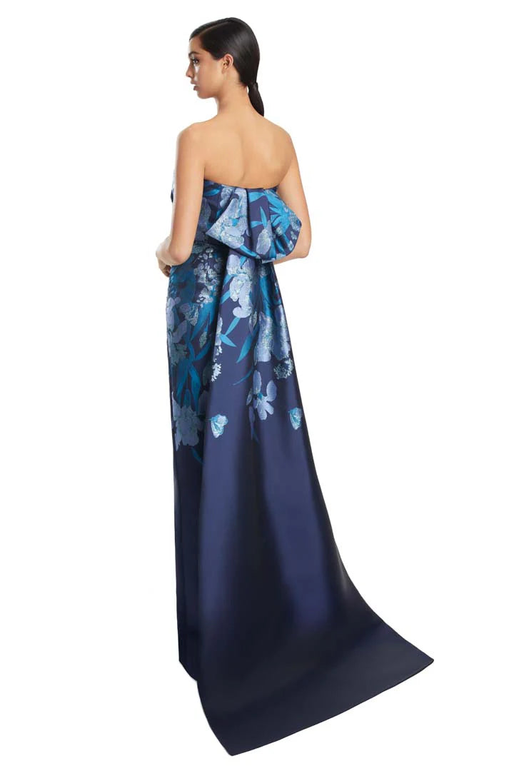 Model wearing Alexander by Daymor 3262S26 strapless floral column gown with draped bodice and statement back detail.