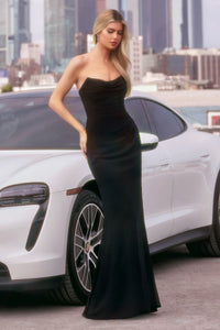 Woman in a black dress standing next to a white car with a cityscape background