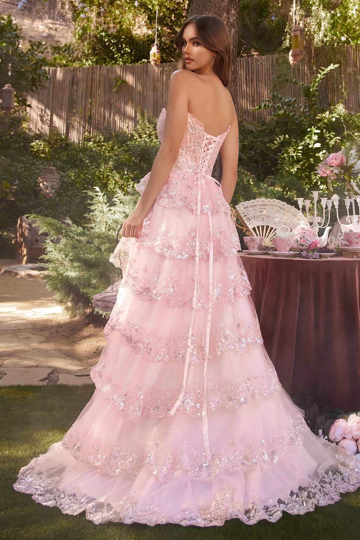 Andrea&Leo A1305 - A sparkling strapless A-line gown with tiered, layered skirt, sparkling scalloped lace hems, sheer boned bodice adorned with glistening sequins, and a lace-up corset back for a captivating look at prom.  The model is wearing the dress in pink.