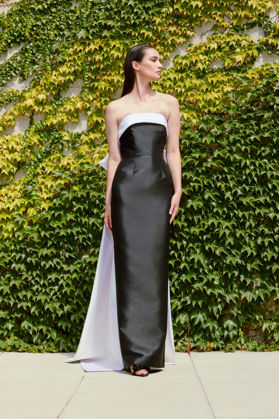 Model wearing Audrey+Brooks 6420 strapless black and white gown featuring a back bow and train.