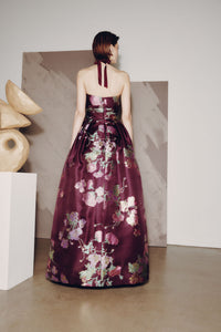 Woman in a floral evening gown standing in a minimalistic room with abstract art.