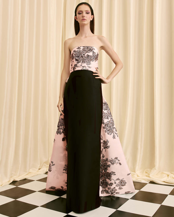 Model wearing a strapless floral top and black and pink gown against a curtain backdrop.