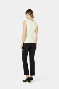 A woman shown from the back wearing a sleeveless cream peplum top, black cropped trousers, and black heels against a light gray studio background.