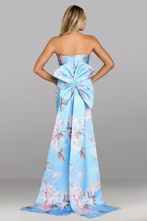 Woman wearing a strapless blue floral dress with a large bow at the back on a gray background