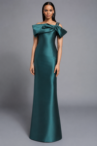 A woman modeling a floor-length off-the-shoulder gown in teal against a neutral gray studio background.