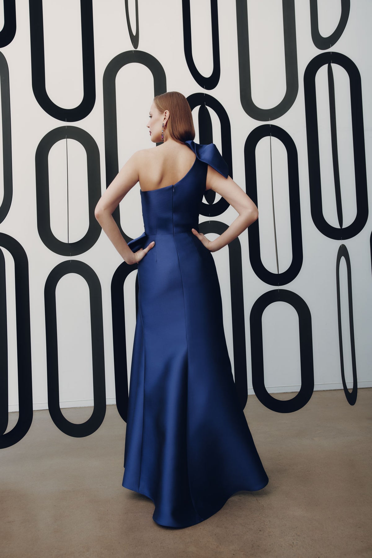 Model wearing Frascara 4927 one-shoulder gown with draped bodice, asymmetrical peplum, and fit-and-flare skirt.  Model is wearing the color amethyst.  Back View.