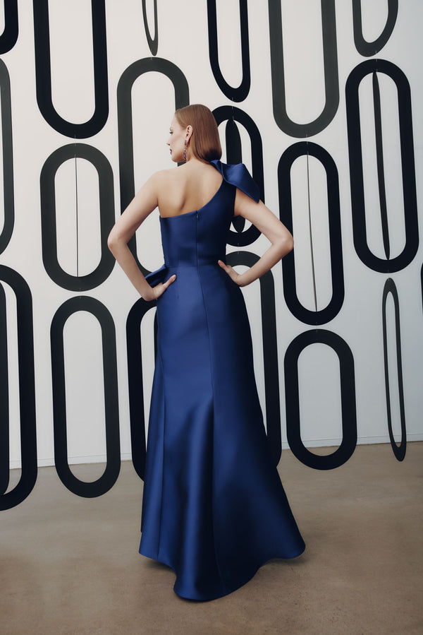 Model wearing Frascara 4927 one-shoulder gown with draped bodice, asymmetrical peplum, and fit-and-flare skirt.  Model is wearing the color amethyst.  Back View.