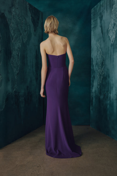 Woman in a boysenberry color strapless gown standing in a dark, textured room.