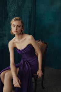 Woman in a boysenberry dress sitting on a chair against a dark teal background