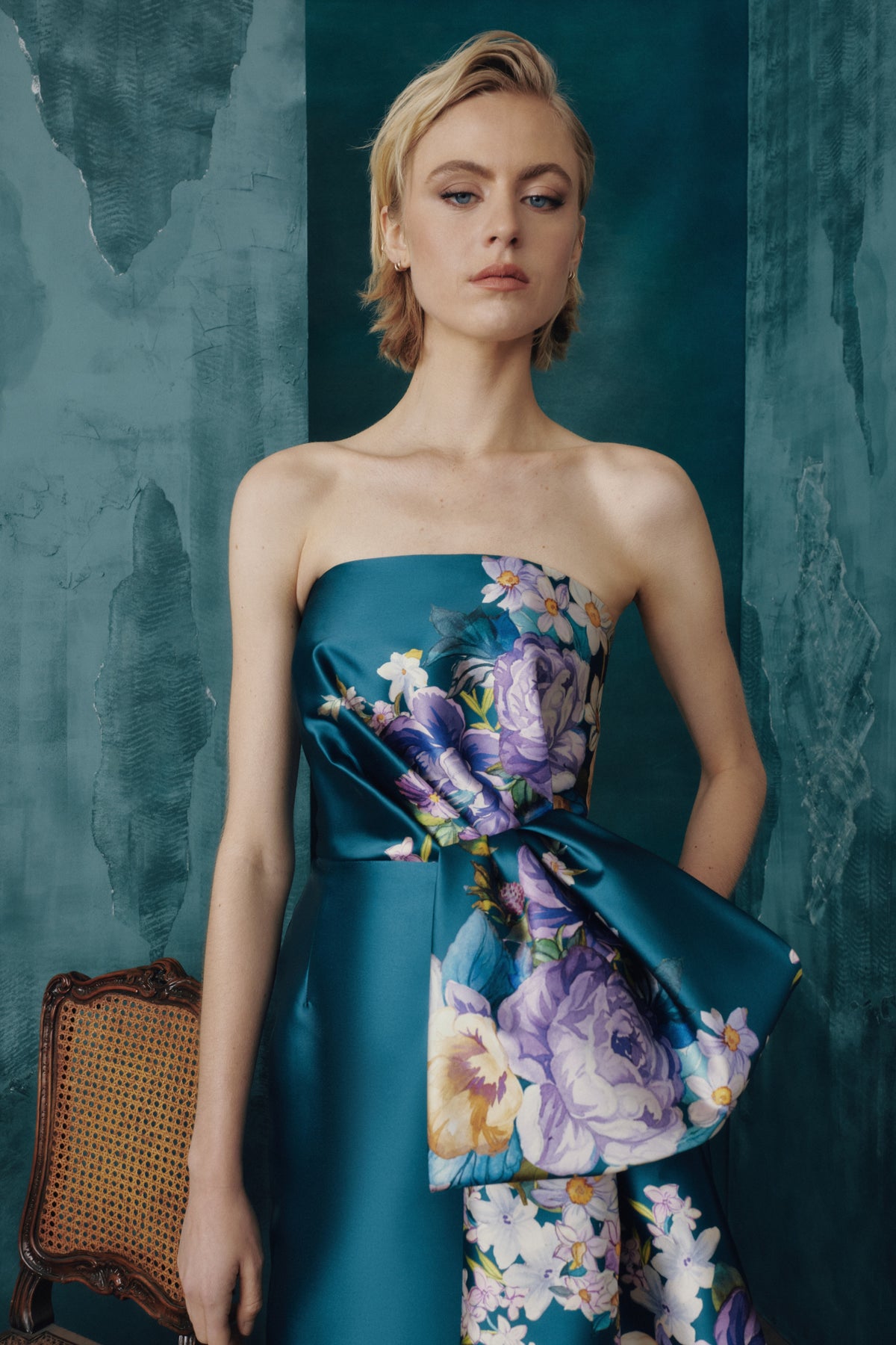 Woman wearing a strapless dress with floral design against a textured teal background