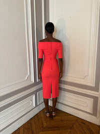 Person wearing a bright red off-shoulder dress standing against a wall with decorative molding.