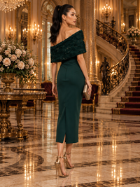 A woman stands in a grand, luxurious hotel lobby wearing a teal color off-the-shoulder midi dress with a textured shawl collar, paired with metallic gold high-heeled sandals and holding a small metallic clutch.