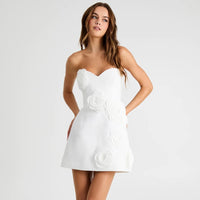 Woman wearing a white strapless dress with floral embellishments on a light gray background