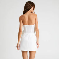 A woman shown from the back wearing a strapless white mini dress with structured corset-style detailing at the waist, photographed against a clean light gray studio background.