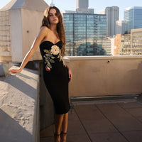 Woman in a black dress with floral embroidery on a rooftop with cityscape background