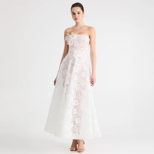A woman modeling a strapless white lace gown with a large floral applique at the bust and a full floor-length skirt, photographed against a clean white studio background.