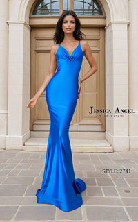 A woman models a bright royal blue floor-length evening gown with a fitted silhouette, deep V-neckline, and a small bow detail at the bust. She stands outdoors in front of a beige stone building with a wooden door.