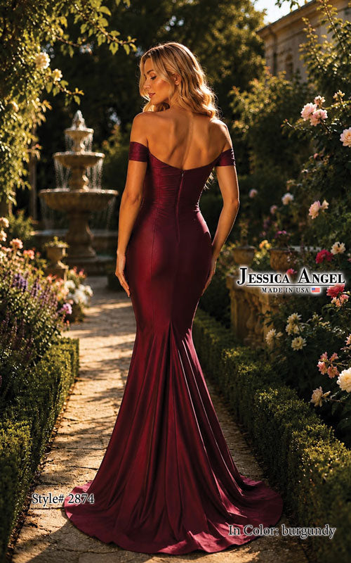 A woman stands in a garden wearing a floor-length burgundy off-the-shoulder mermaid gown, photographed from the back. The dress has a fitted silhouette with a train and structured back.