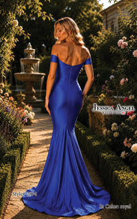 A woman stands in a garden wearing a royal blue off-the-shoulder mermaid gown with a fitted silhouette and long train. The photo is taken outdoors with hedges, flowers, and a fountain in the background.