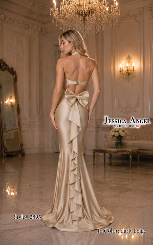 A woman stands in a grand interior wearing a champagne beige evening gown from the back. The dress has a halter-style back with a large bow at the waist, a fitted mermaid silhouette, and cascading ruffle detailing along the lower back and skirt.