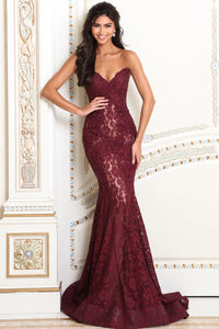 A woman models a strapless burgundy lace mermaid gown with a sweetheart neckline in an ornate cream-colored interior setting.