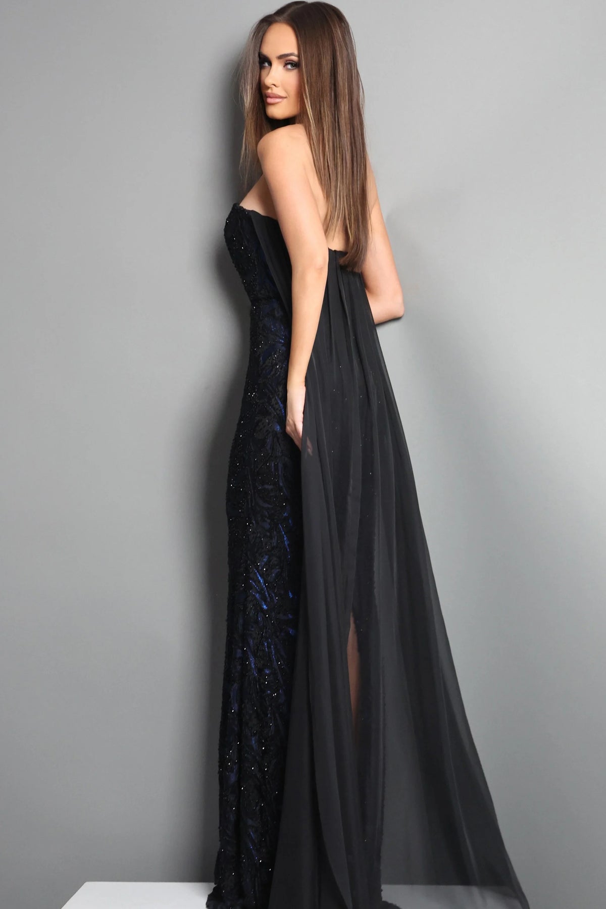 Woman wearing a black evening gown with a sheer overlay against a gray background