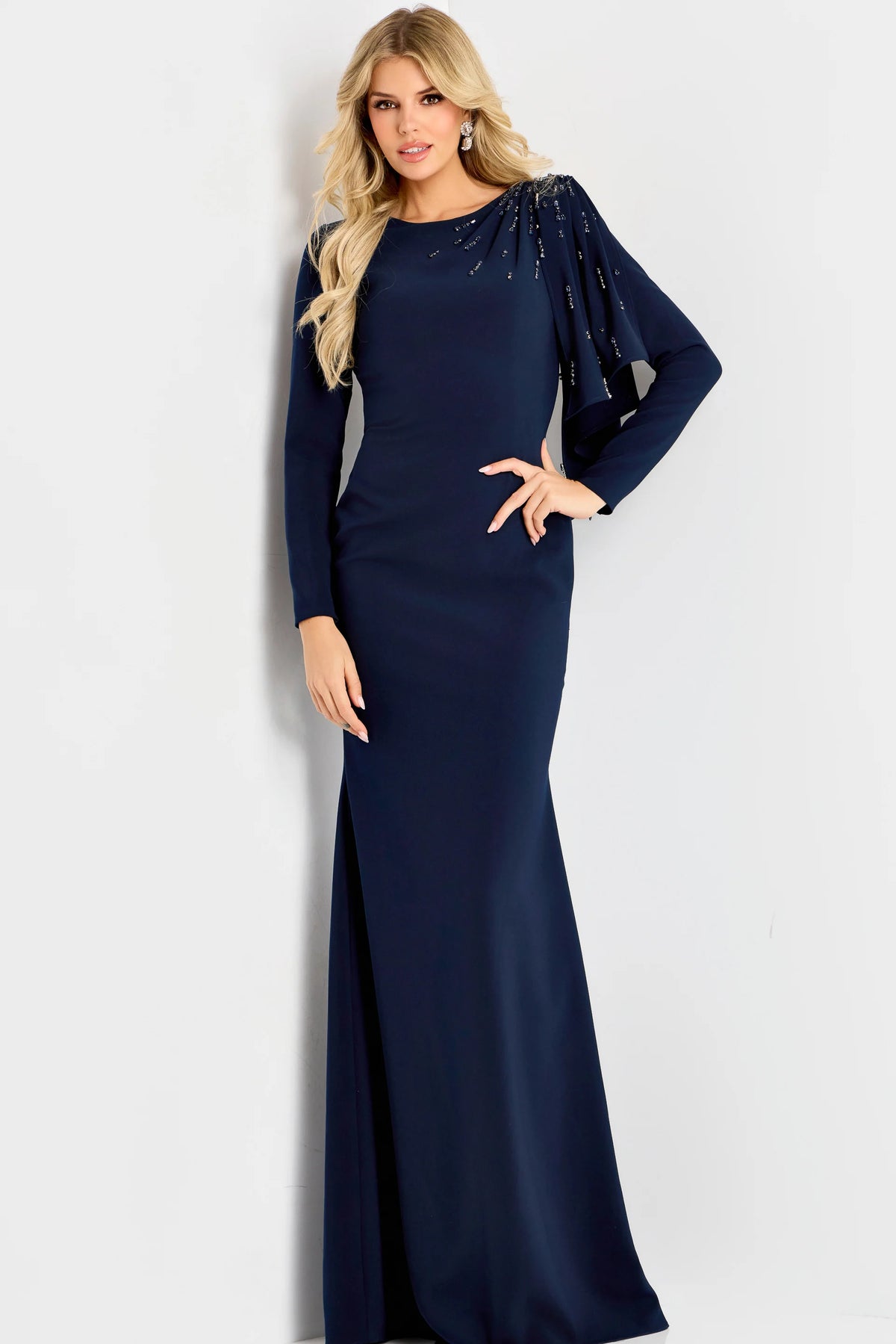 Model wearing Jovani 46738 evening gown featuring a bateau neckline, beaded shoulder detail, long sleeves, and an elegant cape drape.