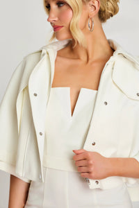 Woman wearing a white outfit with a jacket against a plain background
