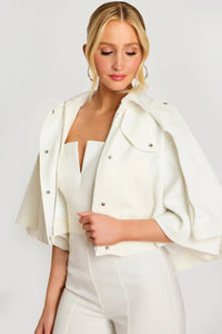Woman wearing a white outfit with a cape-like jacket on a plain background