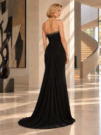 A woman wearing a strapless black evening gown with beaded embellishments on the bodice, photographed from the back in a modern indoor architectural setting with a curved staircase and polished floor.