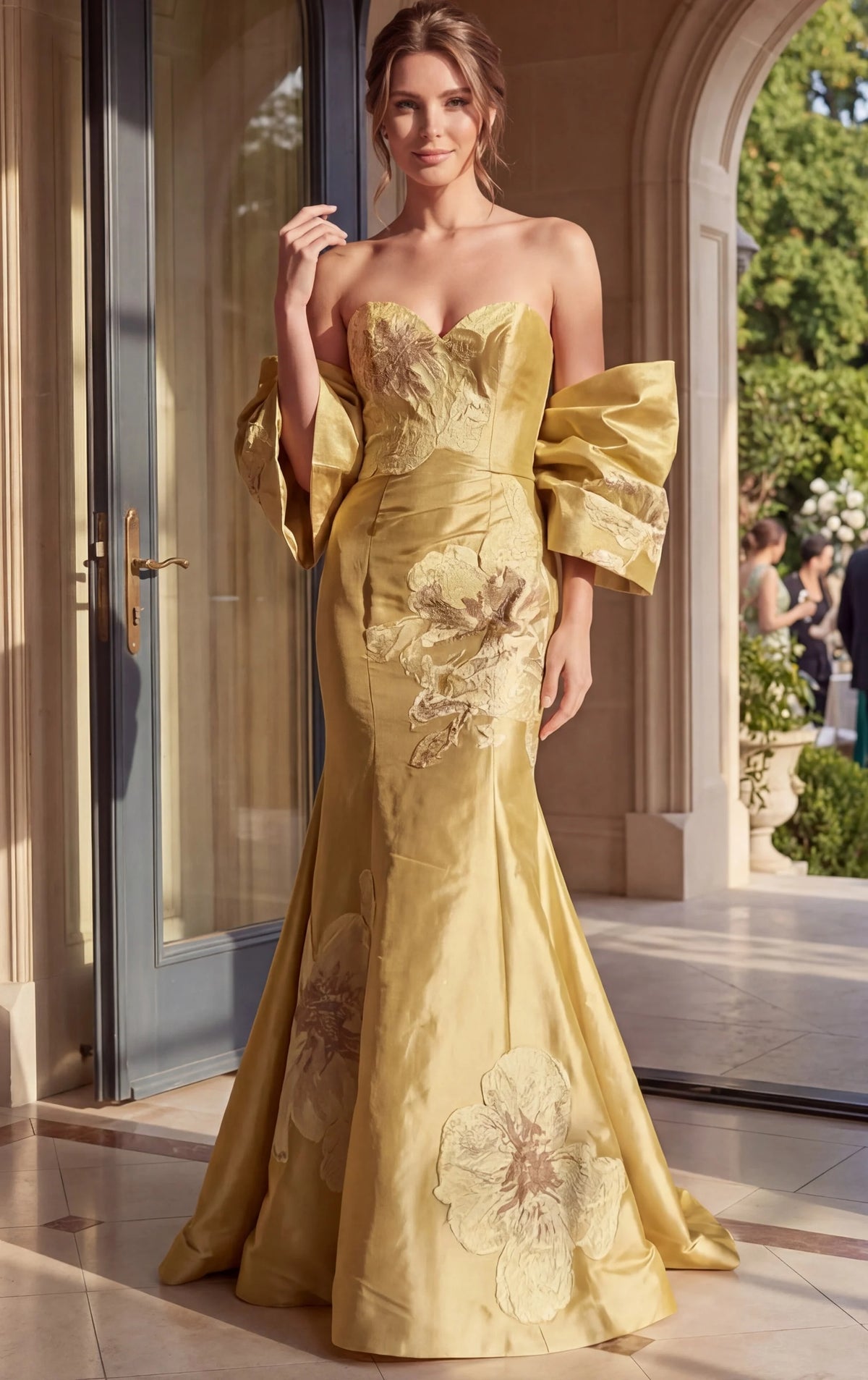 Woman in a yellow evening gown standing in an elegant outdoor setting.