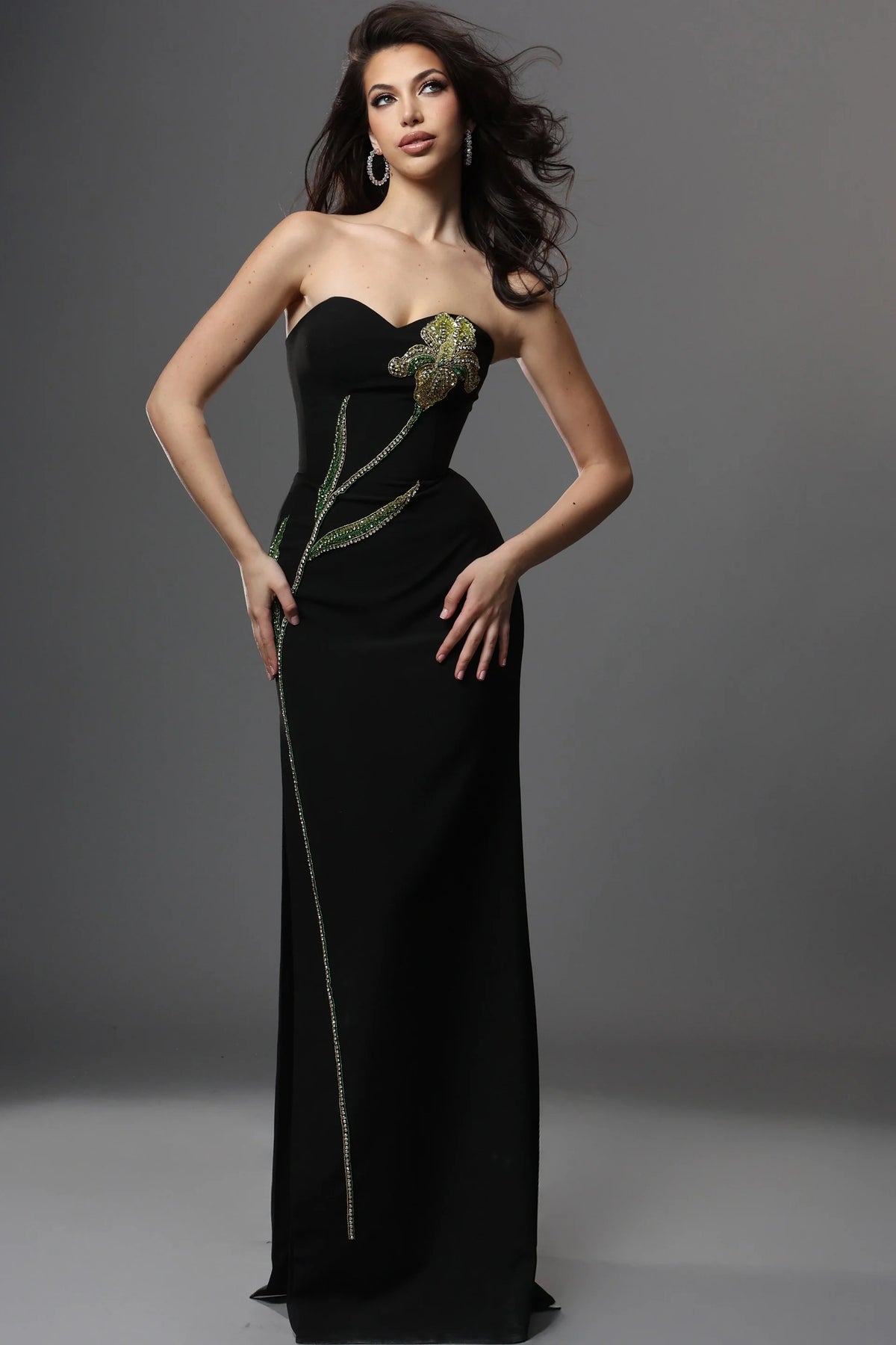 Woman wearing a black strapless gown with floral embellishments on a gray background