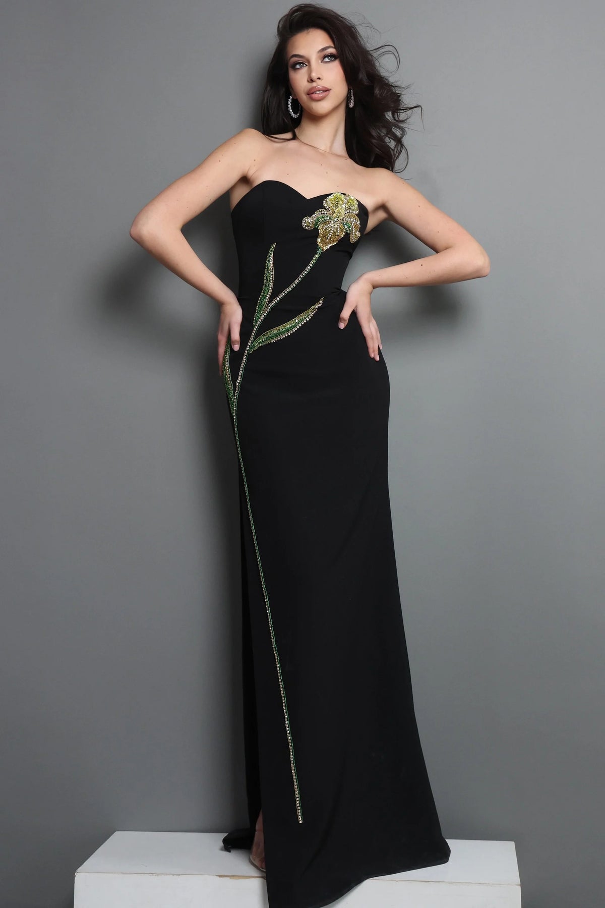 Woman wearing a black strapless gown with floral embellishments against a gray background