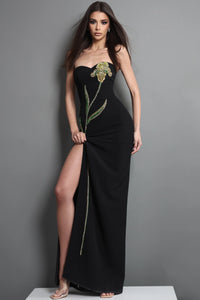 Woman wearing a black dress with floral embroidery against a gray background