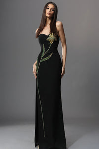Woman wearing a black evening gown with green embellishments on a gray background