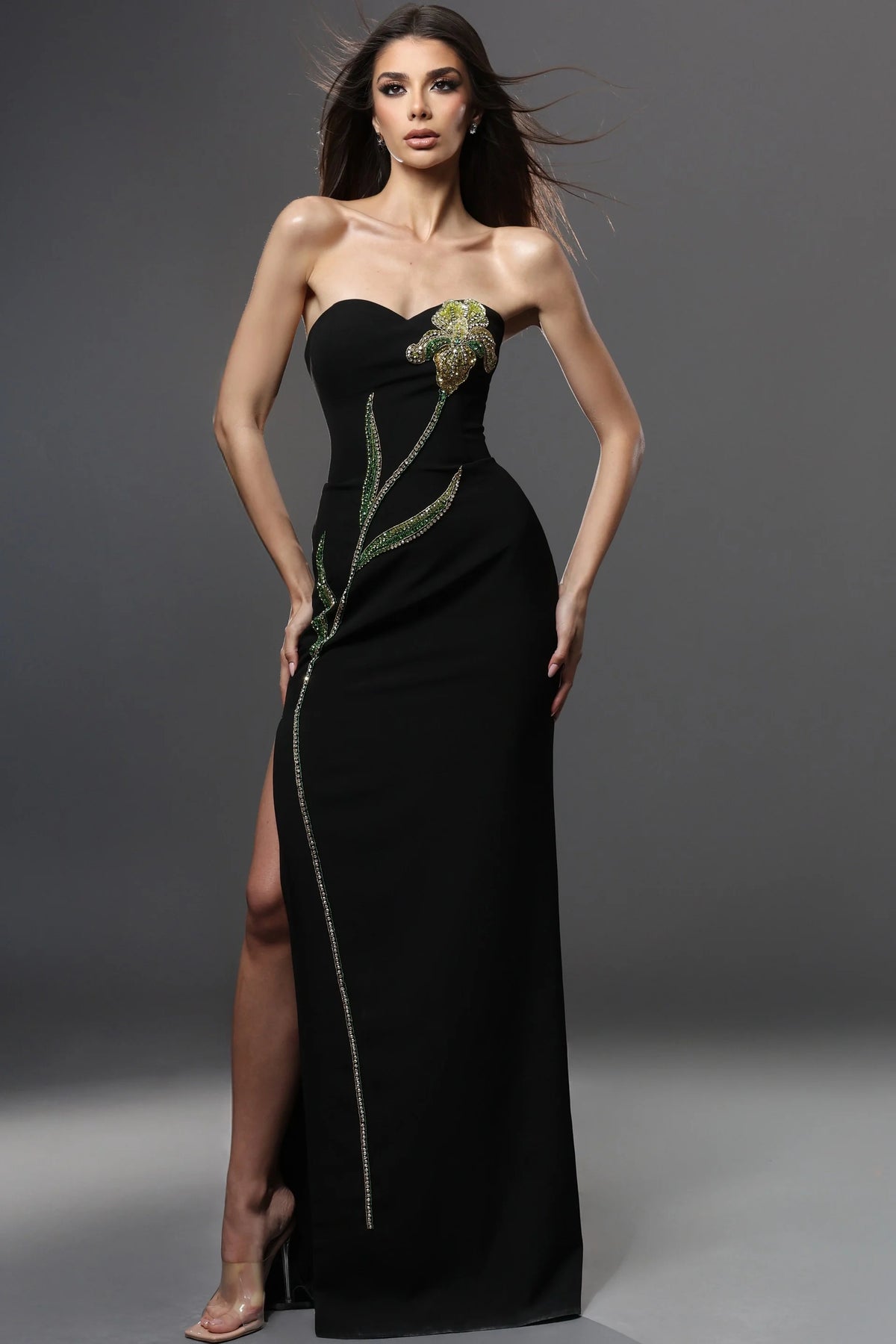 Woman wearing a black strapless gown with floral embellishments on a gray background