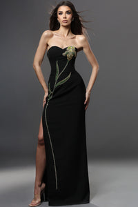 Woman wearing a black strapless gown with floral embellishments on a gray background