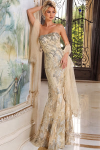 A woman models a strapless champagne beige and silver sequined mermaid gown with a matching sheer draped scarf, set in an elegant interior with a large framed painting and ornate doors.