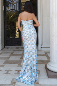 A woman stands with her back to the camera wearing a strapless light blue and silver sequined floor-length gown in an outdoor entryway with columns and a gate.