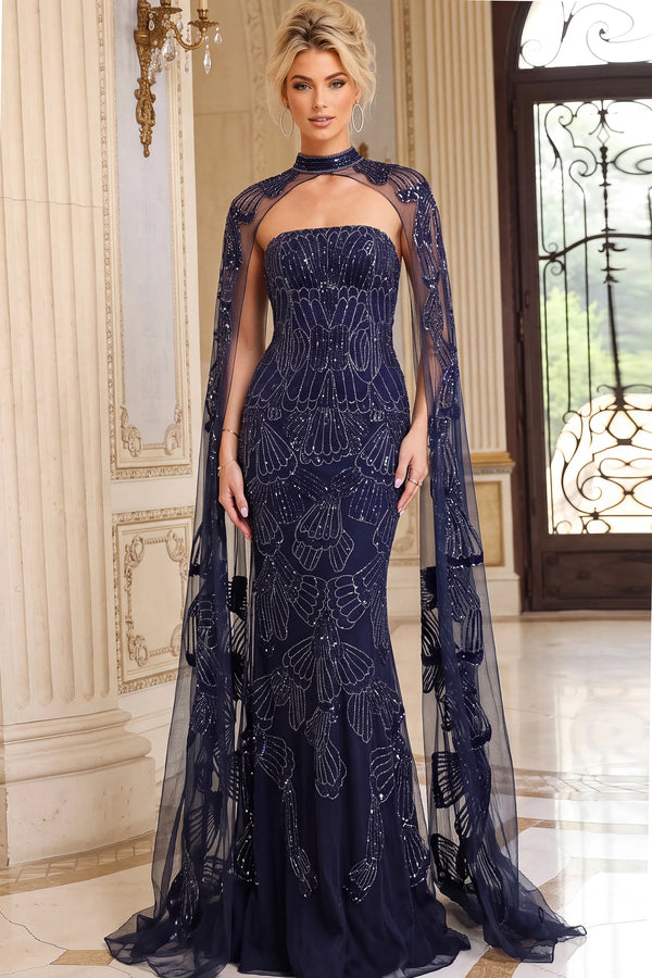 A woman models a floor-length navy blue gown with a high neck, sweetheart neckline, and a sheer draped cape overlay decorated with silver beaded patterns, set in an elegant indoor environment.