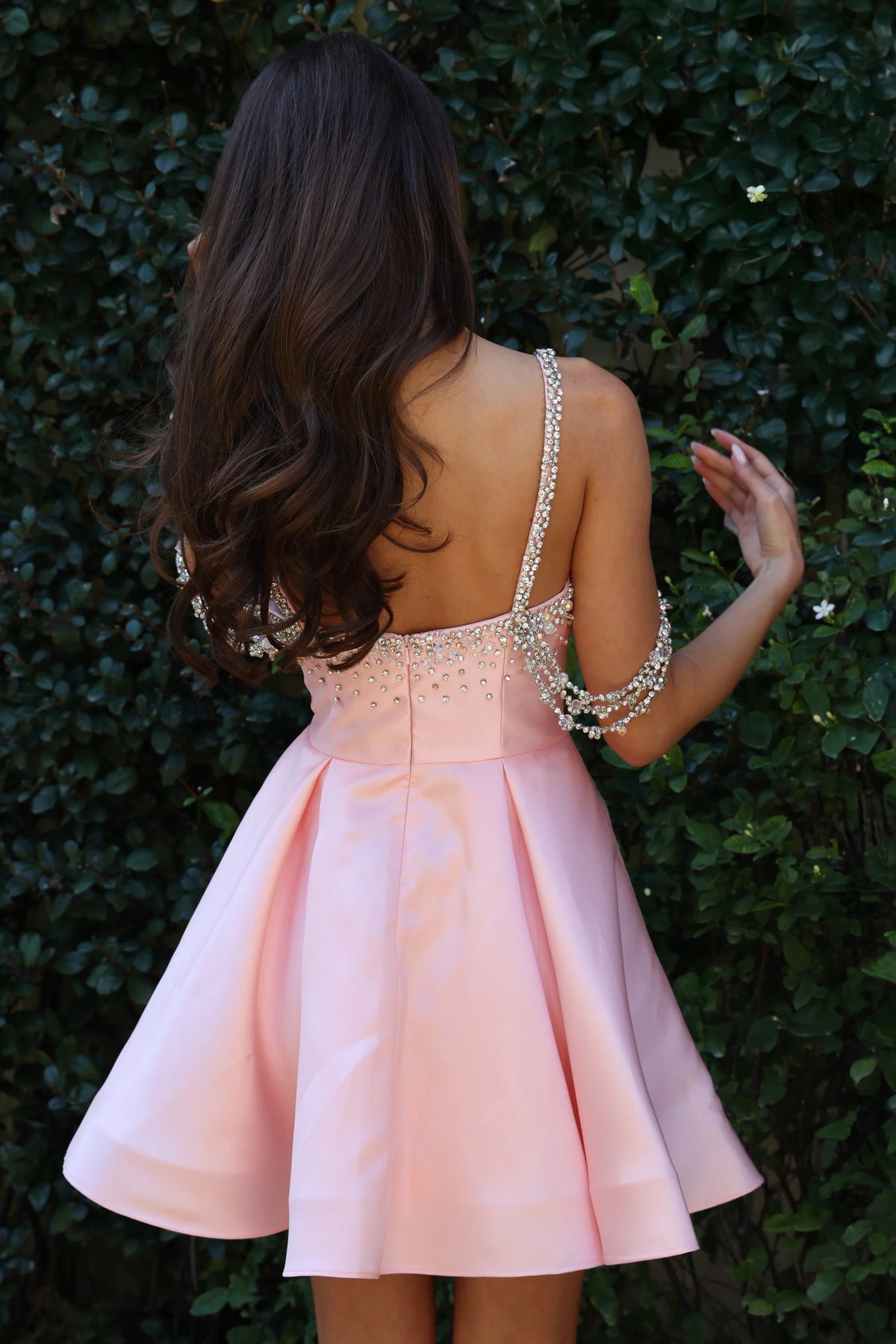Pink dress with embellished straps worn by a person against a green leafy background